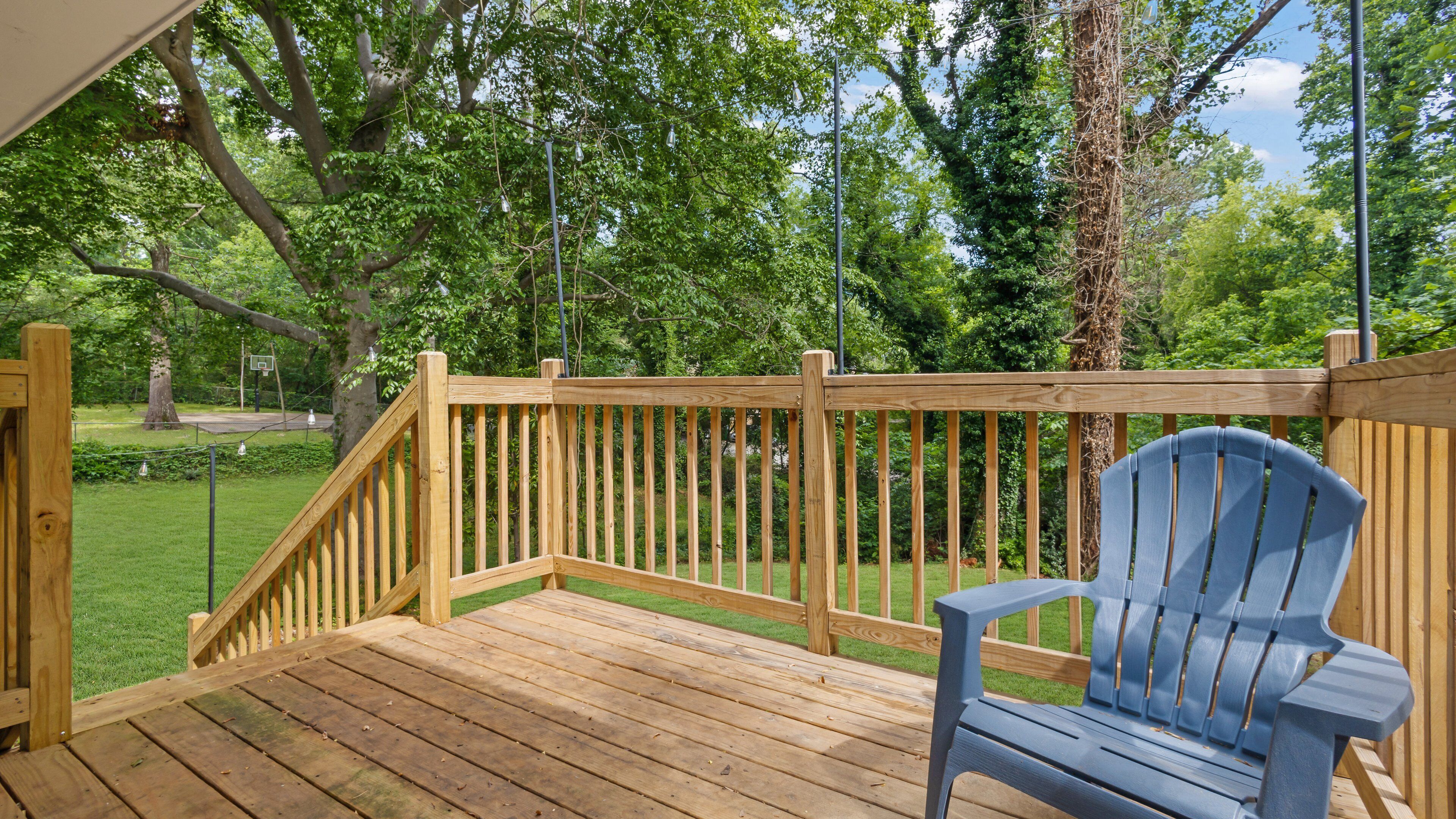 A wooden deck with a blue chair, surrounded by lush greenery and trees.
