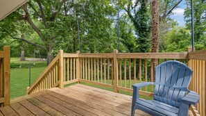 A wooden deck with a blue chair, surrounded by lush greenery and trees.