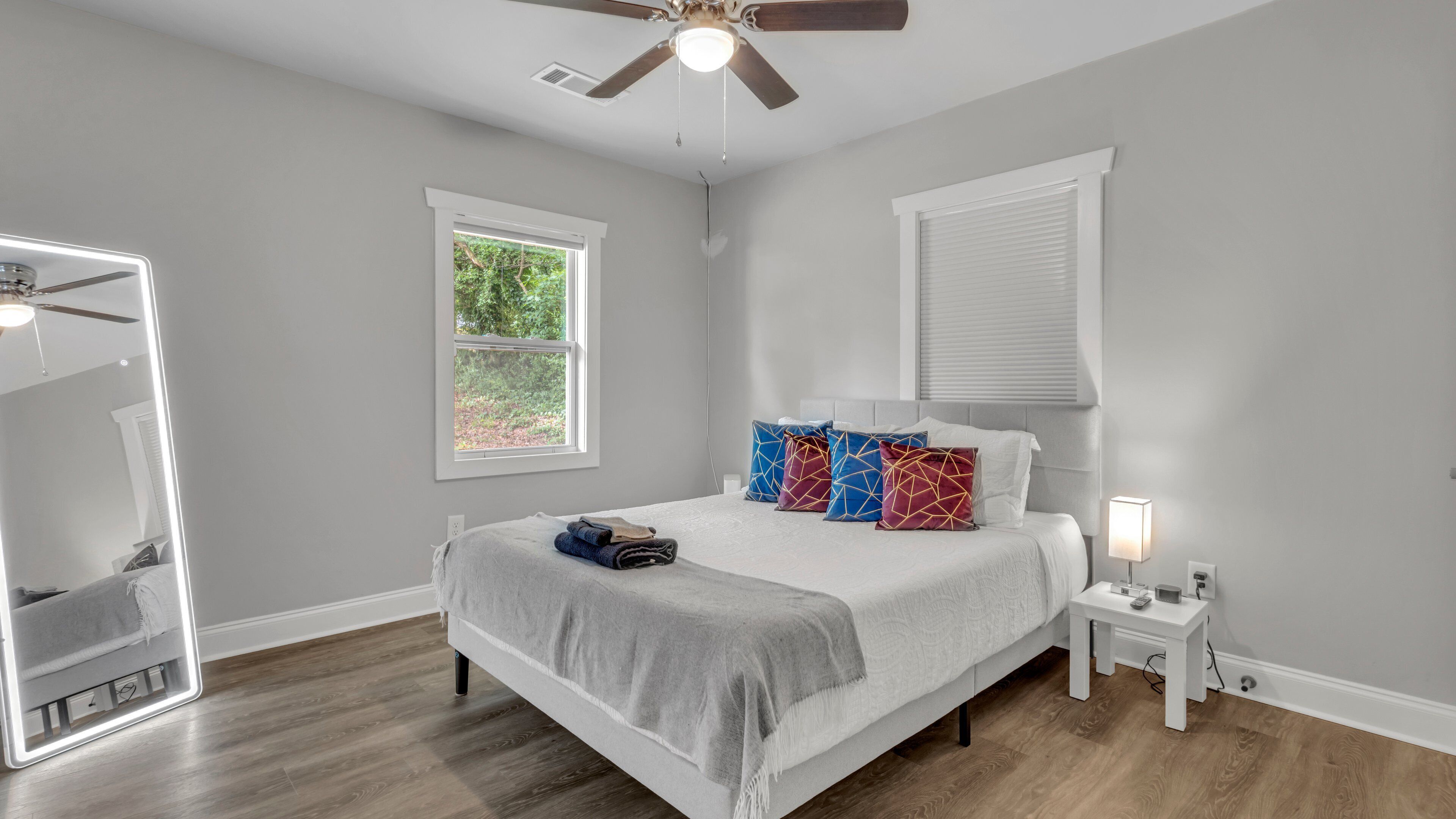 A bedroom with a bed, a ceiling fan, a window, a bedside table, and a nightstand.