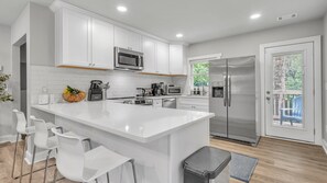 Une cuisine moderne avec des meubles blancs, des appareils en acier inoxydable et un îlot central doté de tabourets de bar.
