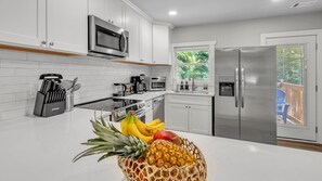 Une cuisine moderne avec des meubles blancs, des appareils en acier inoxydable et un panier de fruits posé sur le plan de travail.