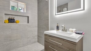 A modern bathroom with a shower, a vanity with a mirror, and toiletries. - Tranquil 3-bedroom house in charming Decatur   Near Attractions! (Decatur)