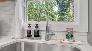 Eine Küche mit einem Edelstahl-Spülbecken, einem Fenster mit Blick auf Bäume und zwei Seifenspendern auf der Arbeitsplatte.