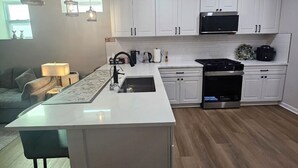 Una cocina moderna con armarios blancos, una isla central, horno empotrado e iluminación colgante.