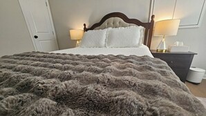 Una cama con un edredón gris esponjoso, un cabecero de madera, dos lámparas de noche y una mesita de noche con un dispensador de pañuelos.