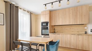 A modern kitchen with wooden cabinets, a built-in oven, and a dining area with a table and chairs. - Luminous apartement 1BDR/4P - Centre de Paris (Paris)