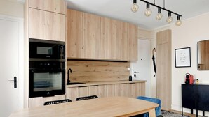 A modern kitchen with wooden cabinets, a built-in oven, and a dining area with a table and chairs. - Luminous apartement 1BDR/4P - Centre de Paris (Paris)