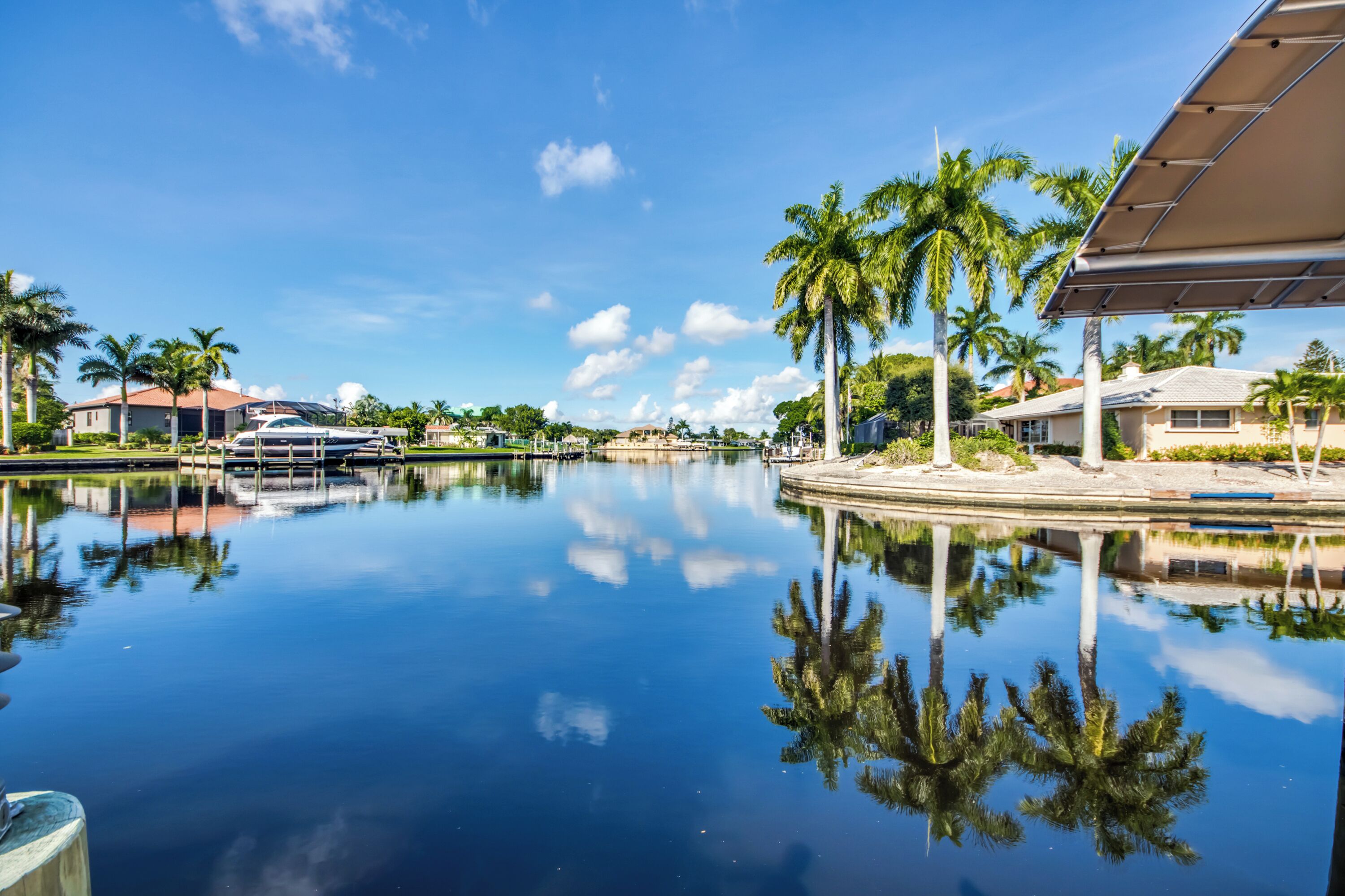 A calm water body reflecting palm trees and buildings, with a clear sky.