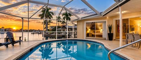 A swimming pool with a glass ceiling, a sunset view, and a dining area with chairs.
