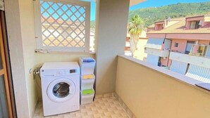 Un balcón pequeño con lavadora, cestas de ropa apiladas y vistas a edificios vecinos.
