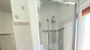 Cabina de ducha con paredes de vidrio, cabezal de ducha de mano y grifo empotrado.
