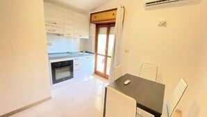 Una cocina compacta con armarios blancos, encimera negra y un comedor con mesa y sillas.