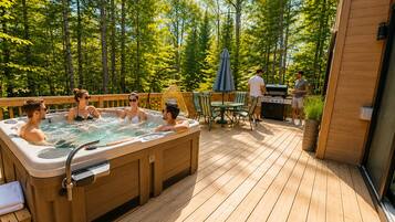 A deck with a hot tub, outdoor seating, and a grill area surrounded by trees.