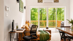 En moderne stue med et træskrivebord, en behagelig sofa, et spisebord og en stor skydedør, der fører ud til en balkon med gelænder af træ.
