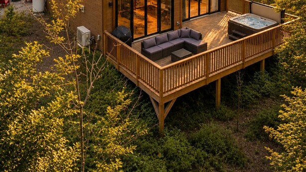 En moderne hytte med to etager og en terrasse, omgivet af skov.