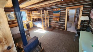 Ein rustikales Blockhaus-Interieur mit Holzausbau, Kamin, Etagenbett und Schreibtisch.