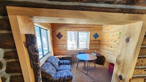 Ein Holzblockhaus-Interieur mit einer Couch, einem runden Tisch und zwei Fenstern.