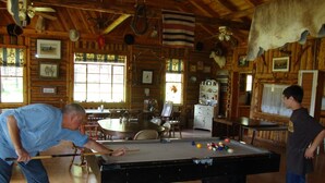 Ein Billardtisch in einer rustikalen Lodge mit Holzwänden, einem Klavier und verschiedenen gerahmten Bildern.