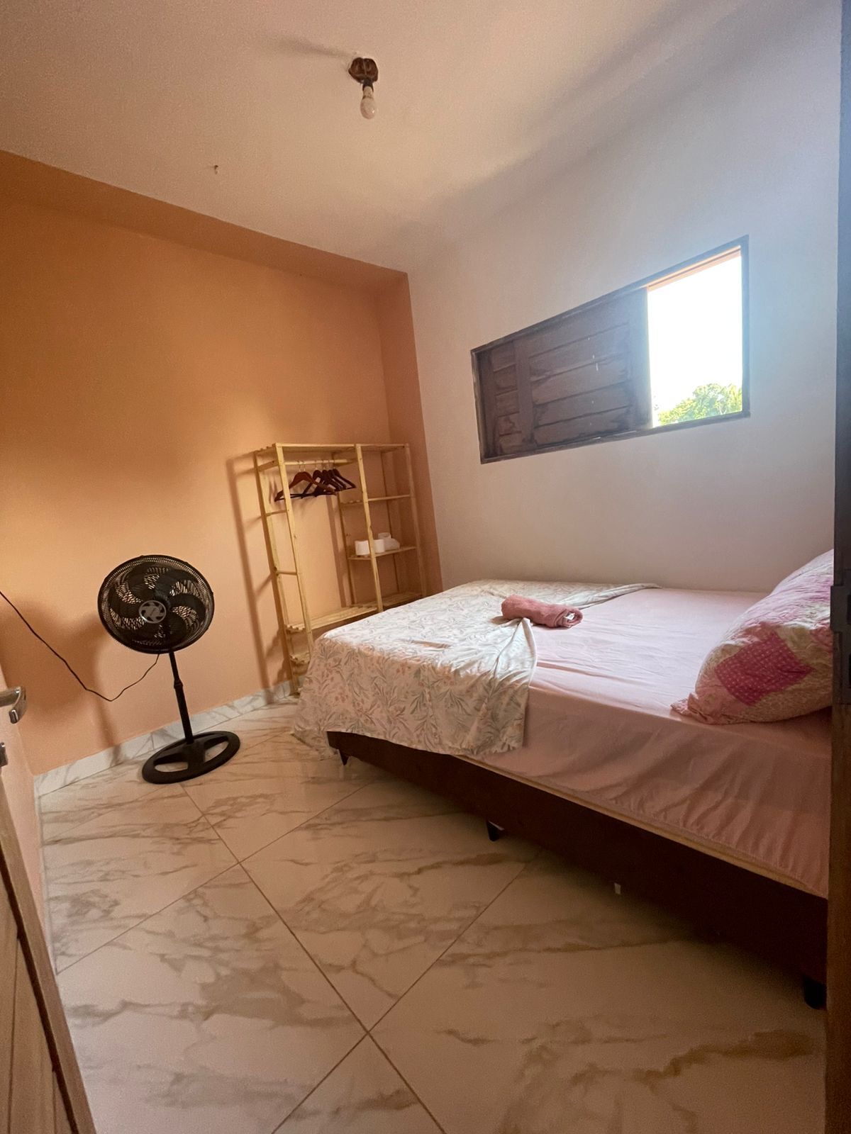 Een slaapkamer met een bed, een ventilator, een raam en een houten garderobe.