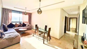 Una sala de estar moderna con un sofá, una mesa de comedor y sillas. Hay dos lámparas colgantes y un ventanal con cortinas.
