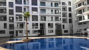 Un edificio moderno con piscina central, varios balcones y una palmera.