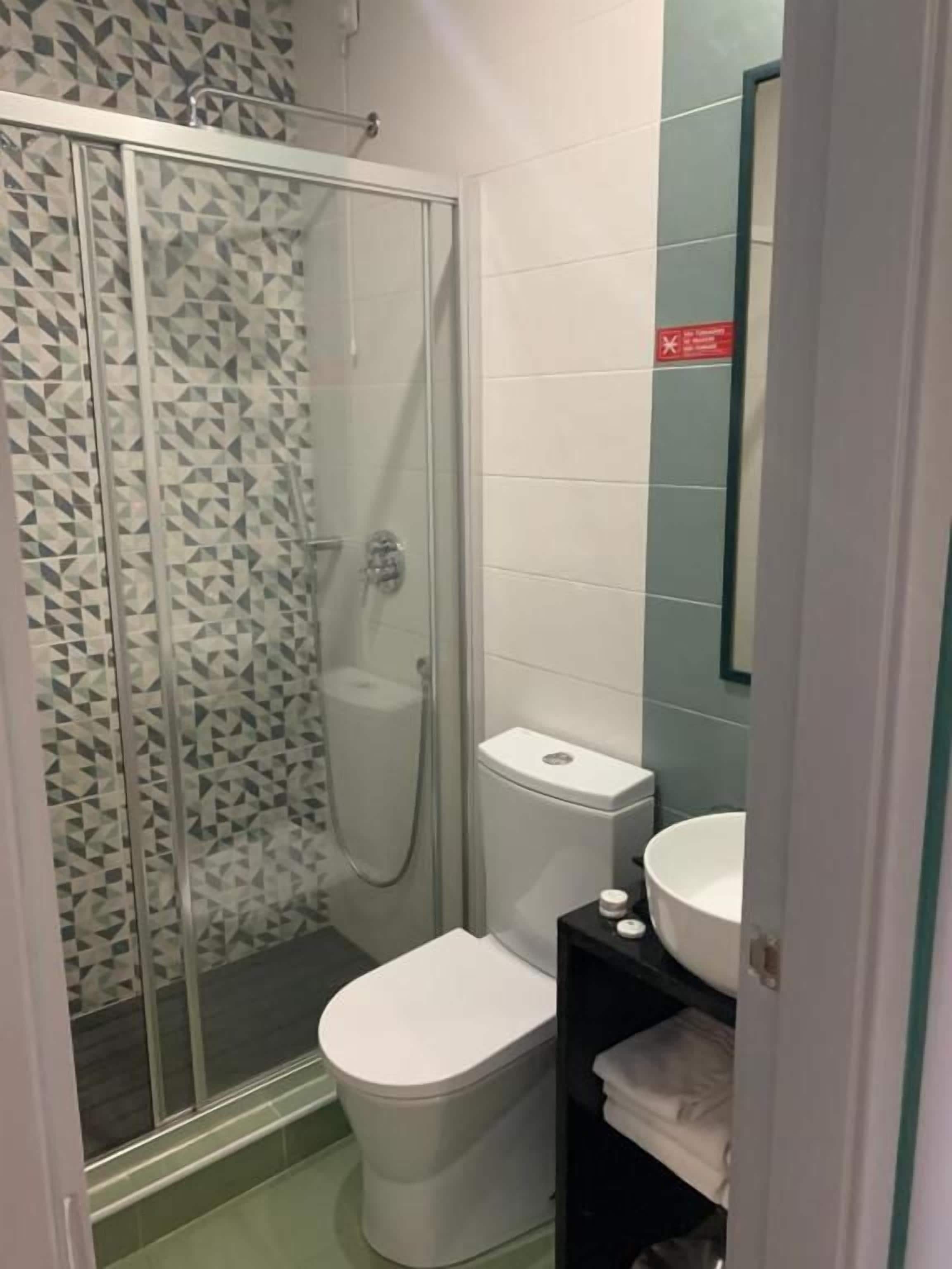 A bathroom with a glass shower enclosure, a toilet, and a sink.