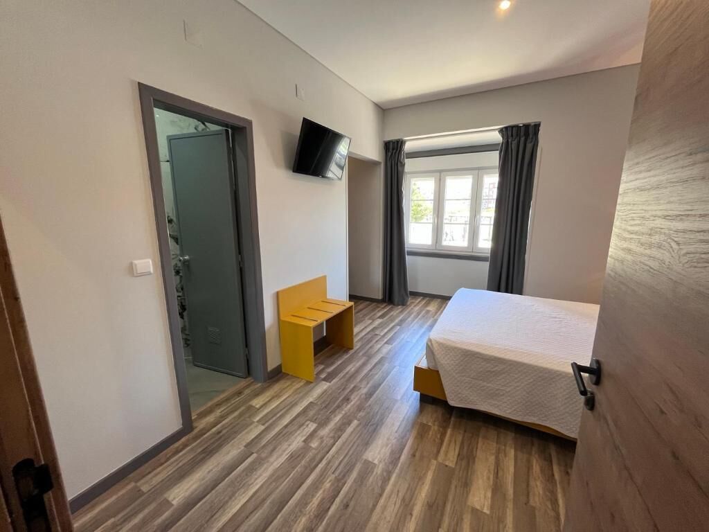 A modern hotel room with a bed, a small seating area, a television, and a window with curtains.
