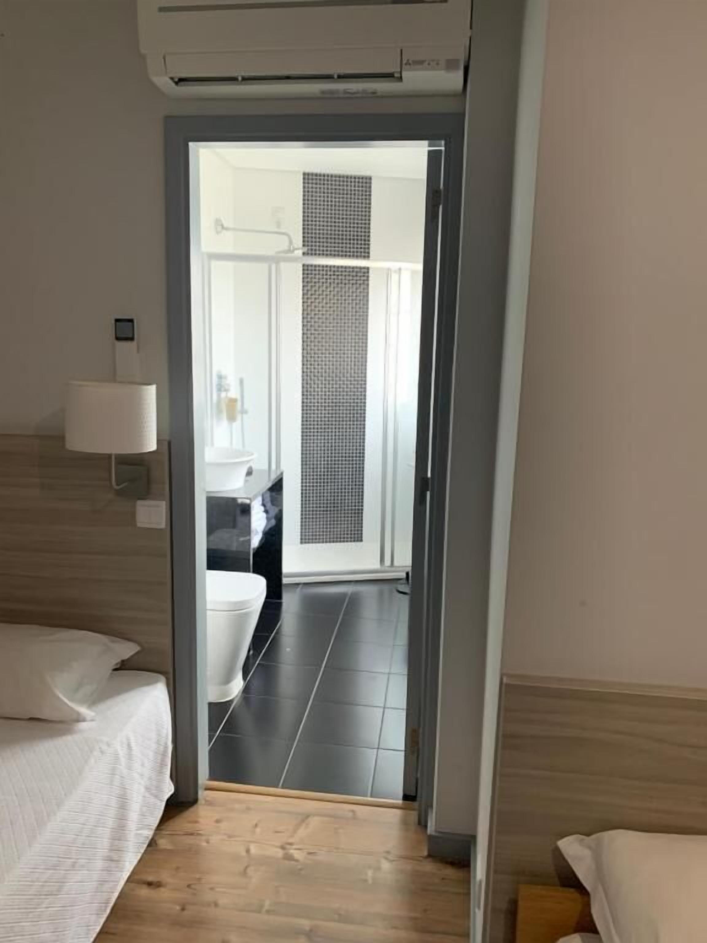 A hotel room with a bed, a bedside lamp, and a view of the bathroom through an open door.