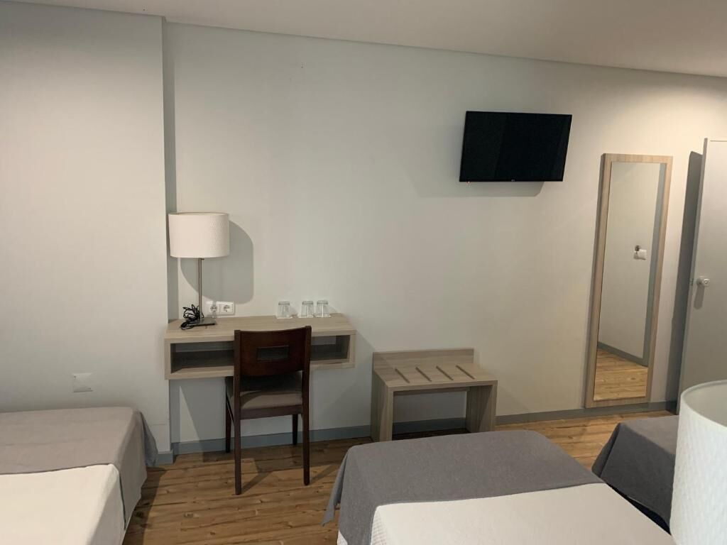 A hotel room with a bed, a desk with a chair, a TV, and a mirror.