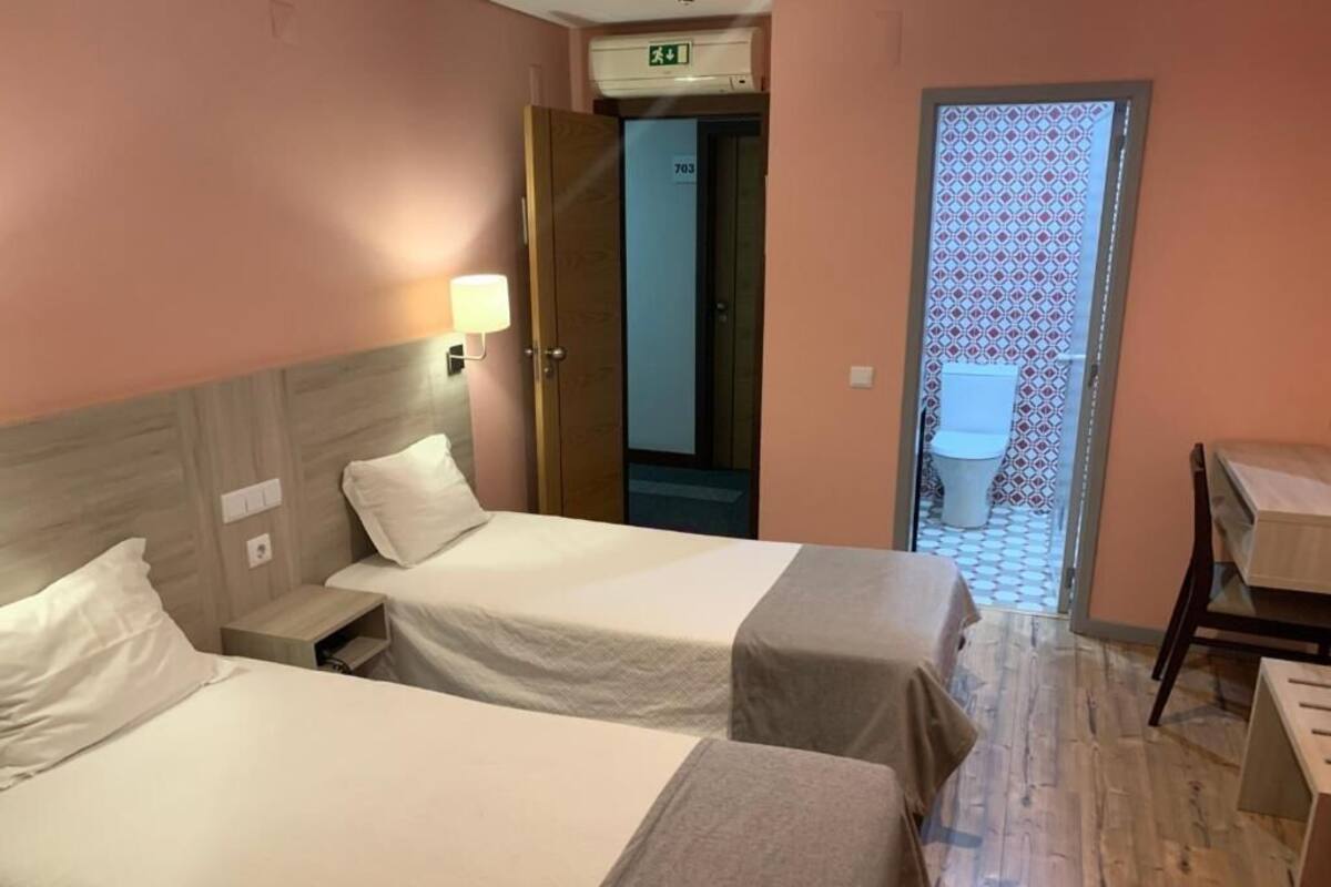 A hotel room with two beds, a desk, a chair, a bathroom, and an exit door.