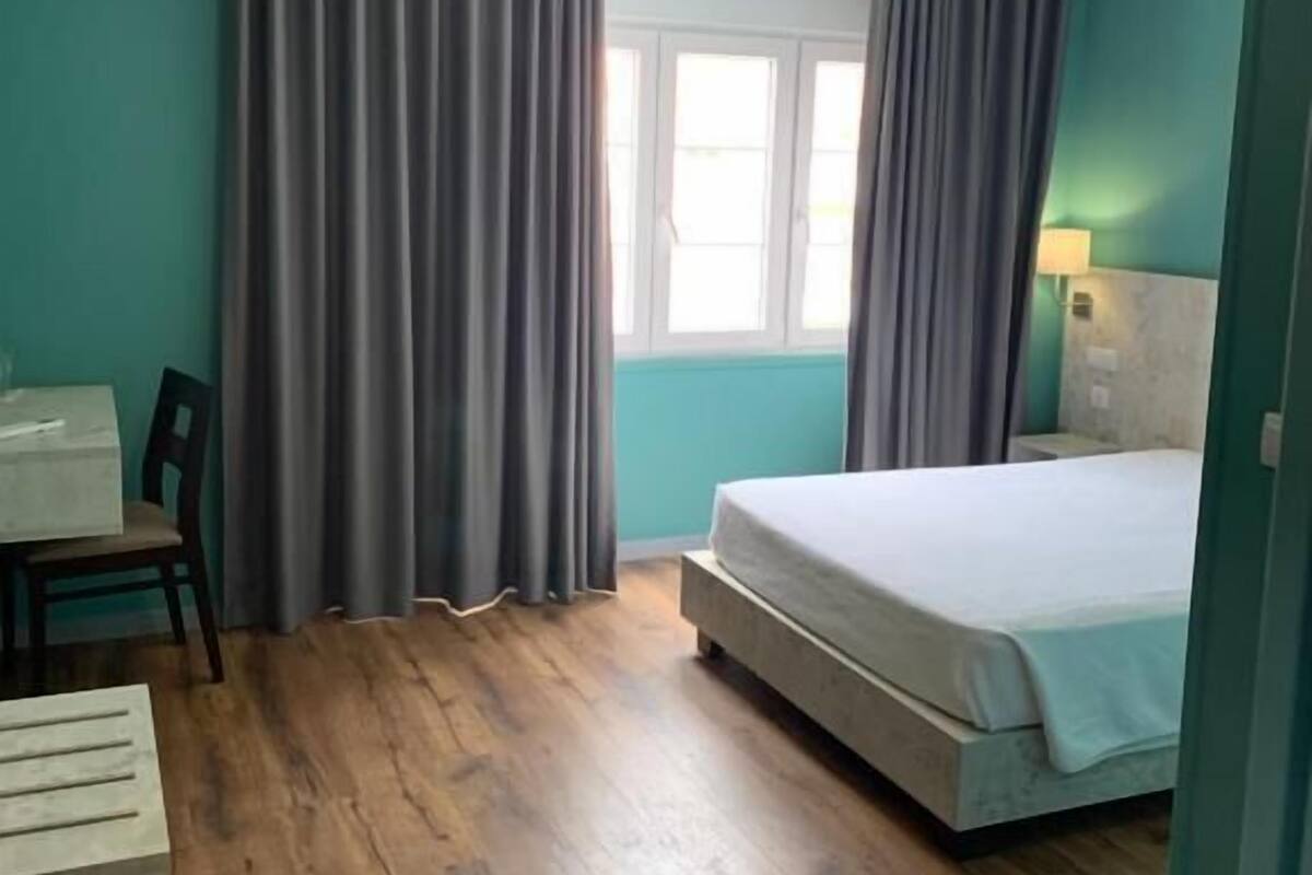 A room with a bed, a desk, and a window with curtains.