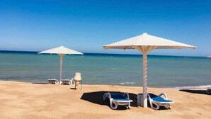 Ein Strand mit zwei weißen Sonnenschirmen und Liegestühlen.