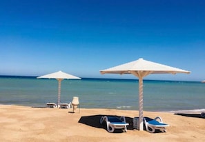 A beach with two white umbrellas and lounge chairs. - Selena bay resort villa 5 BR in Hurghada (Hurghada)