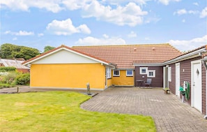 A two-story house with a yellow exterior and a red-tiled roof. There is a paved driveway leading to the house, and a small garden area in front.