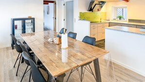 A modern kitchen with a large island, a dining area with a wooden table and chairs, and a small refrigerator. - Cozy home in Nykøbing M with WiFi (Nykøbing M)