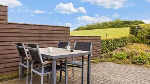 A table and chairs set against a wooden wall with a view of a green field and trees. - Cozy home in Nykøbing M with WiFi (Nykøbing M)