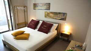 Een opgemaakt bed met twee kussens, een nachtkastje met een lamp en een kunstwerk aan de muur.