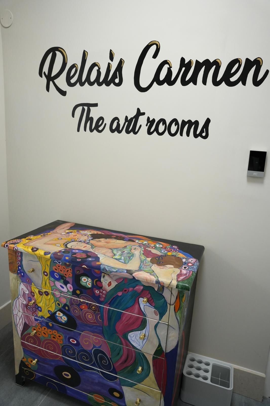 A room with a colorful cabinet and a wall sign that reads "Relaís Carmen The art rooms".
