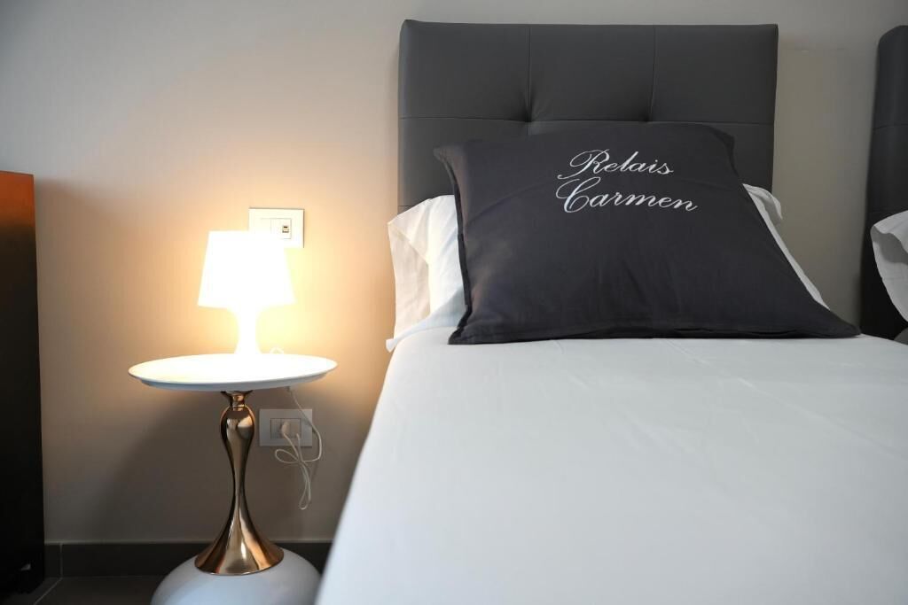 A hotel room with a bed, a bedside lamp, and a pillow with text.