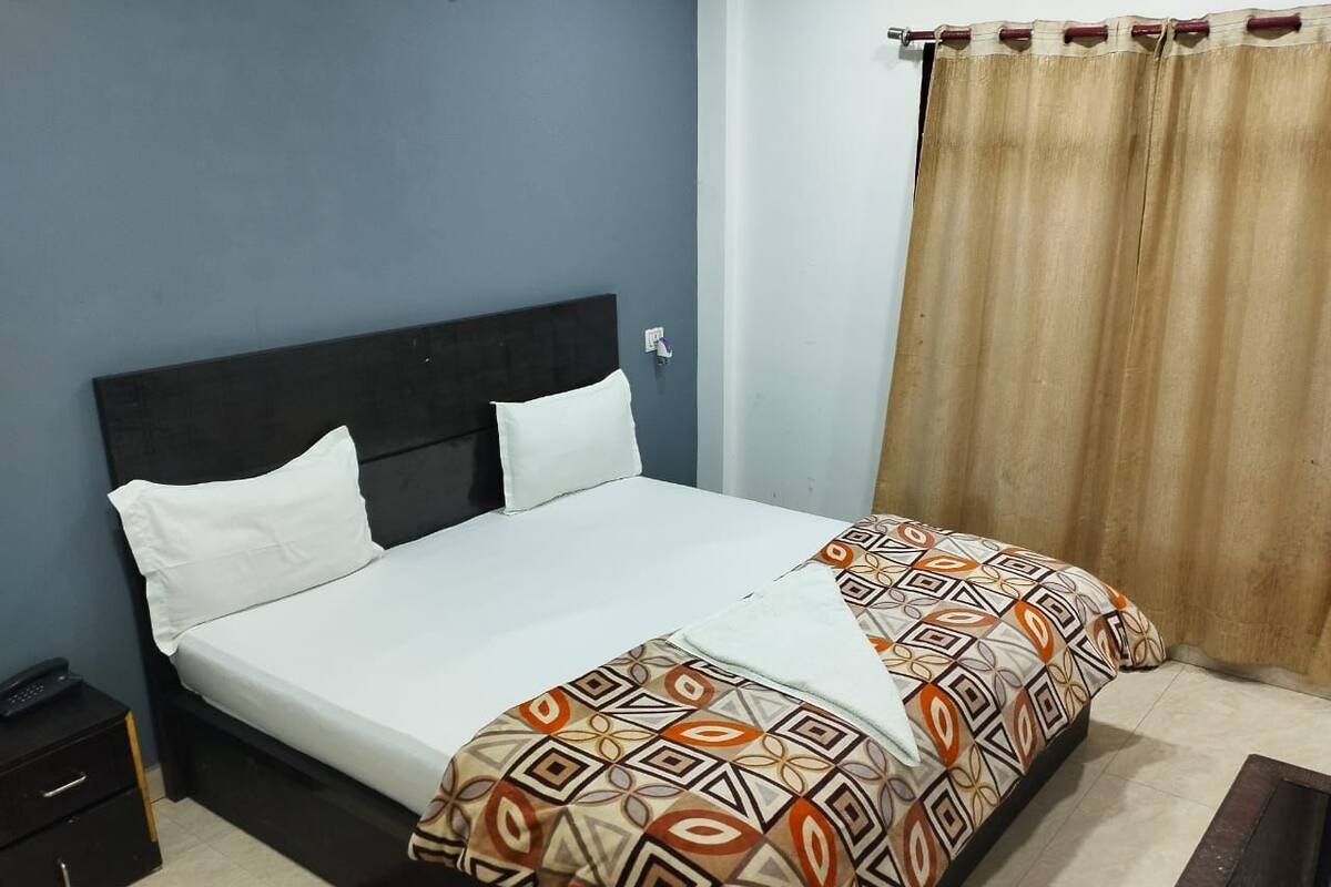 Un lit simple avec une couvre-lit à motifs, une tête de lit sombre, une table de chevet et un rideau.
