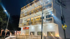 A multi-story hotel with balconies, illuminated windows, and a sign indicating a restaurant. - Hotel Vallabh Palace (Misrikh)