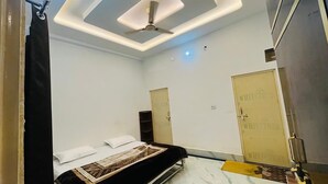 A bedroom with a bed, a ceiling fan, a wardrobe, and a door. - Hotel Vallabh Palace (Misrikh)