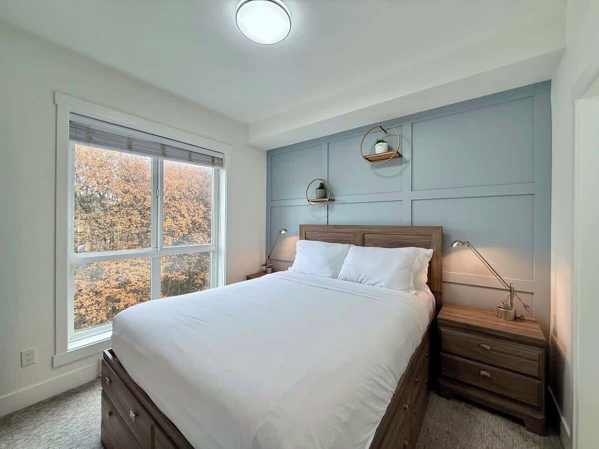 A bedroom with a large bed, bedside tables, a window with a view of trees, and a ceiling light.