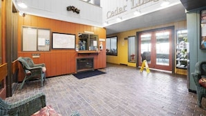 Een lobby met een receptiebalie, rieten stoelen, een open haard en een bord met de tekst 'Welcome to Cedar Lodge'.