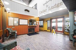 A lobby with a reception desk, wicker chairs, a fireplace, and a sign reading "Welcome to Cedar Lodge".