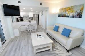 Una cocina moderna con armarios blancos, un refrigerador de acero inoxidable y un televisor de pantalla plana sobre la encimera.