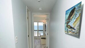 Un corridoio stretto con pavimento in legno chiaro, pareti bianche e una lampada a soffitto. Si vede un quadro di una balena sulla parete destra.