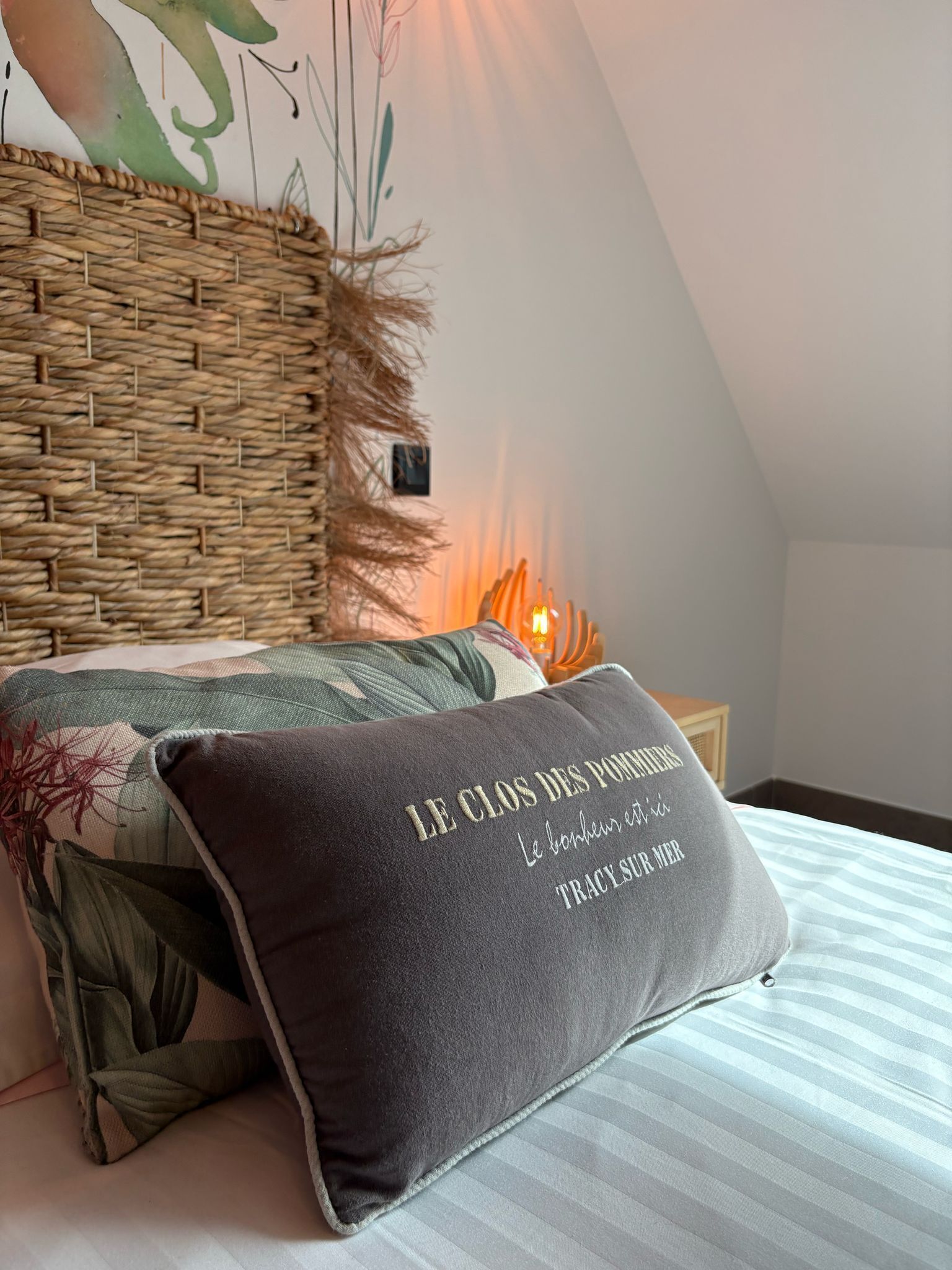 Ein Schlafzimmer mit einem Bett, einem gewobenen Kopfteil, einem Zierkissen und einer Wandleuchte.