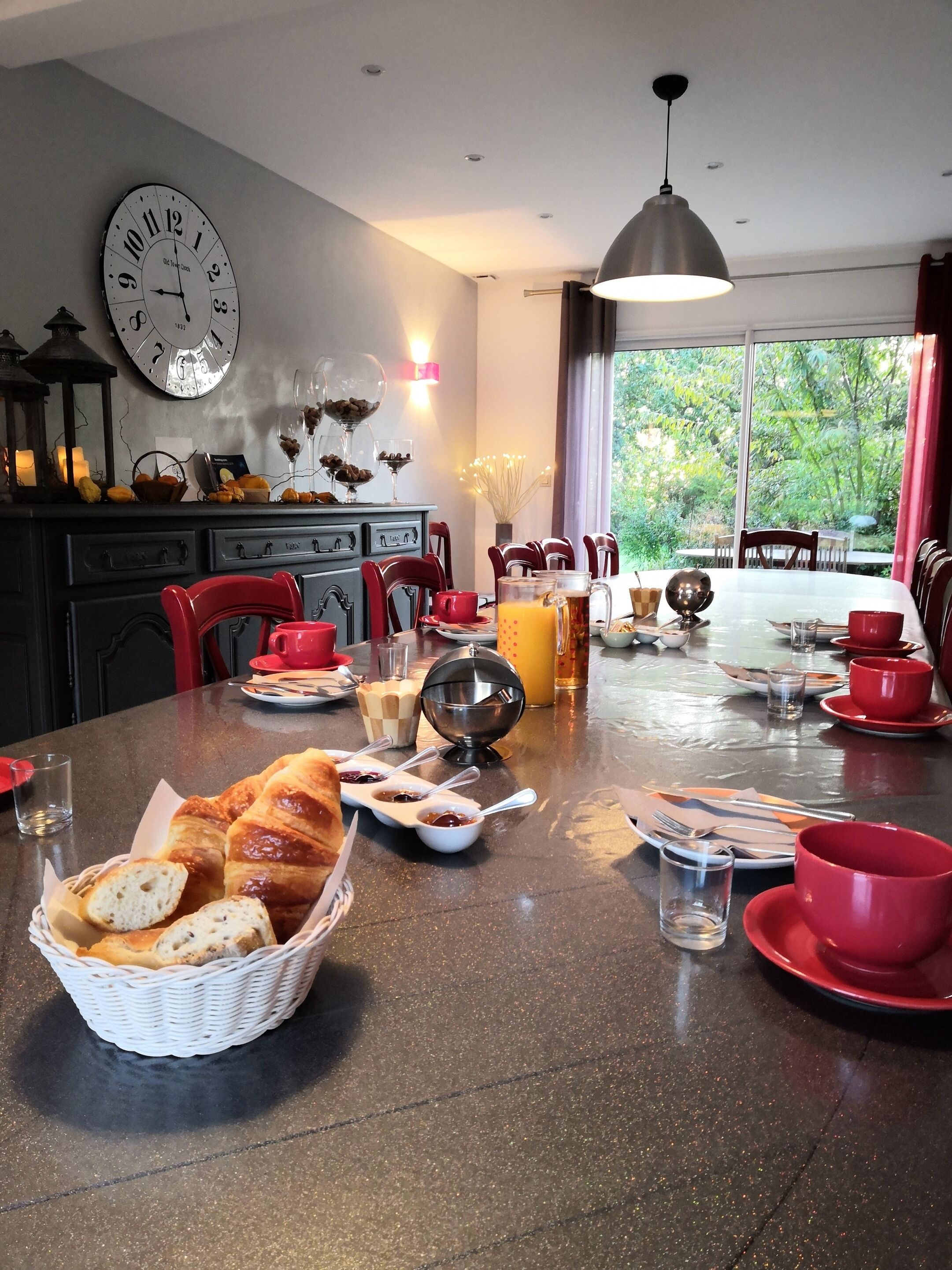 Un coin repas avec une table ronde mise pour un repas, comprenant du pain, des condiments et des gobelets rouges.