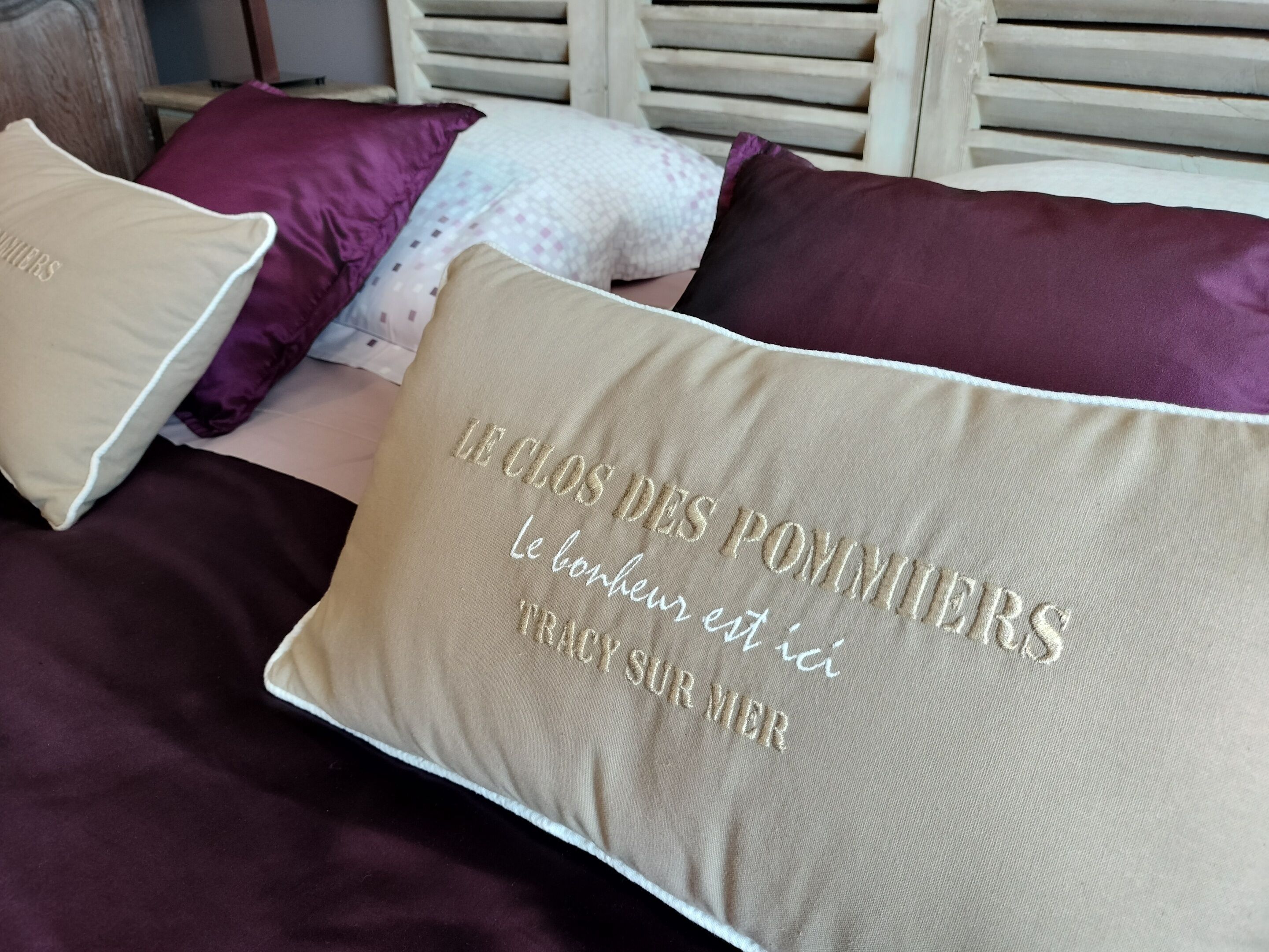 Uma cama com vários travesseiros, incluindo um bordado com texto em francês.